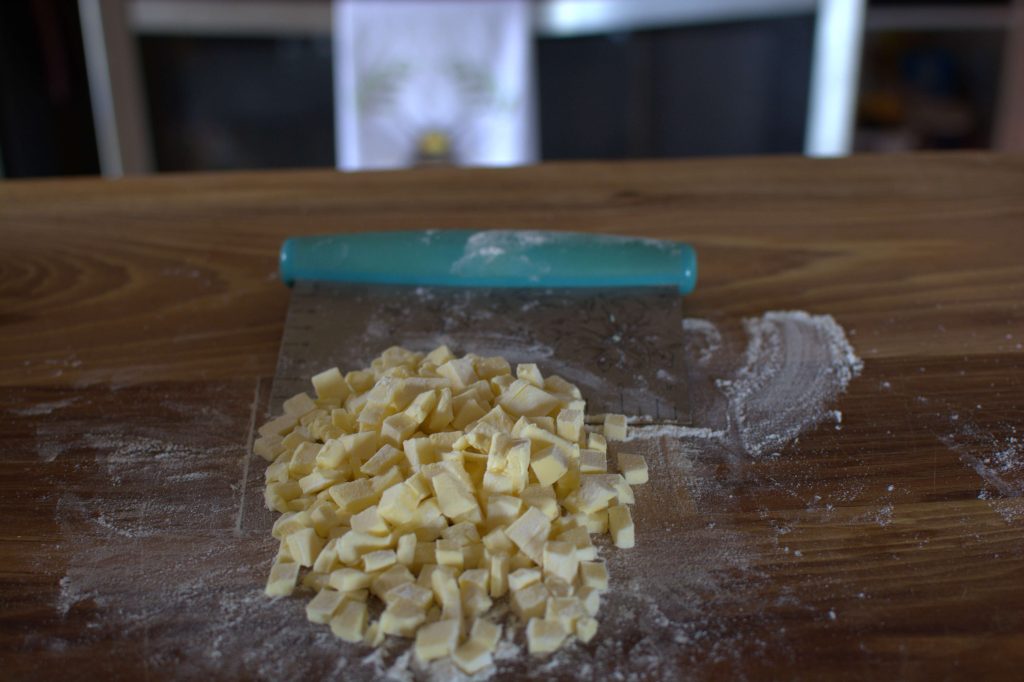Butter cut into cubes on a cutting board against a dough scraper