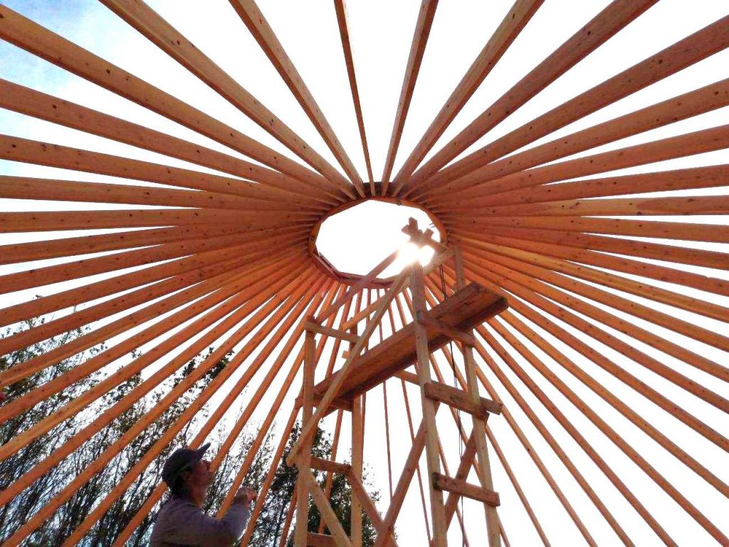 Scaffolding in the center of a yurt with now walls and a man looking up at the open dome.