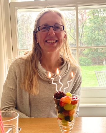 Woman sitting at a table in front of a window with a fruit dessert and candles