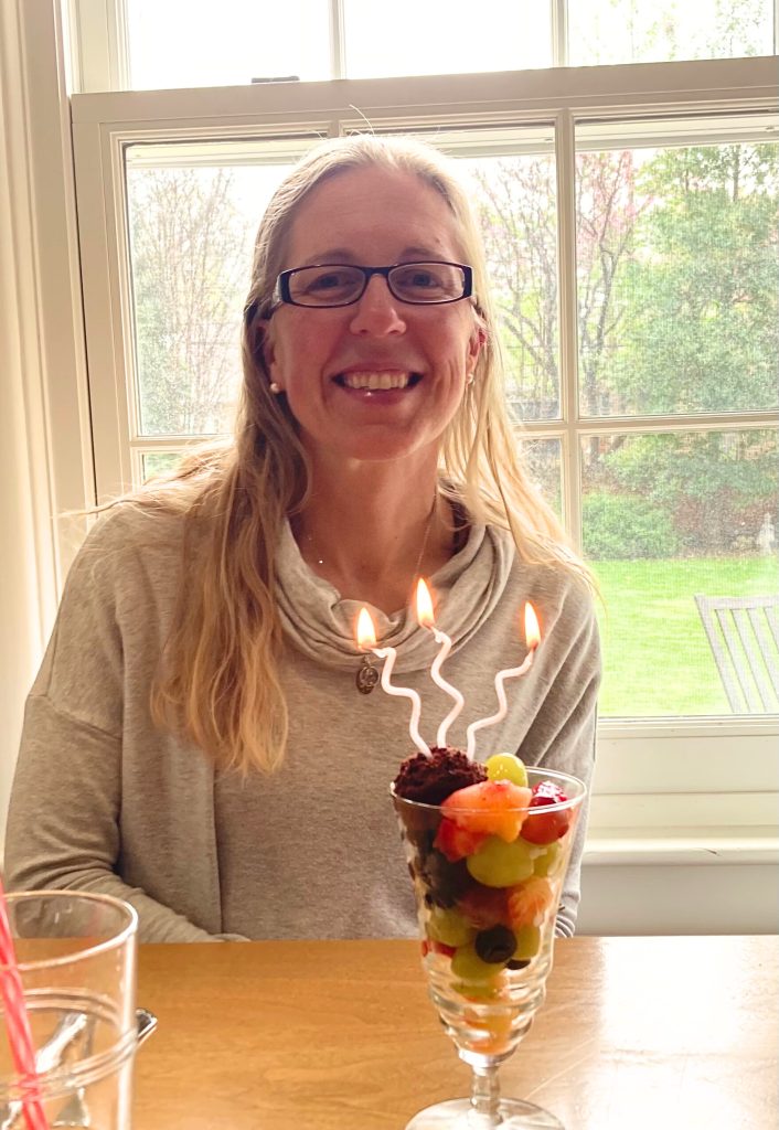 Forty year old woman sitting at a table in front of a window with a fruit dessert and candles for her birthday