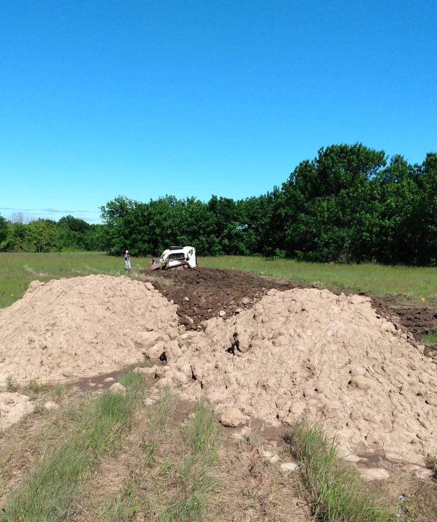 Skid steer working in mud with piles of dirt