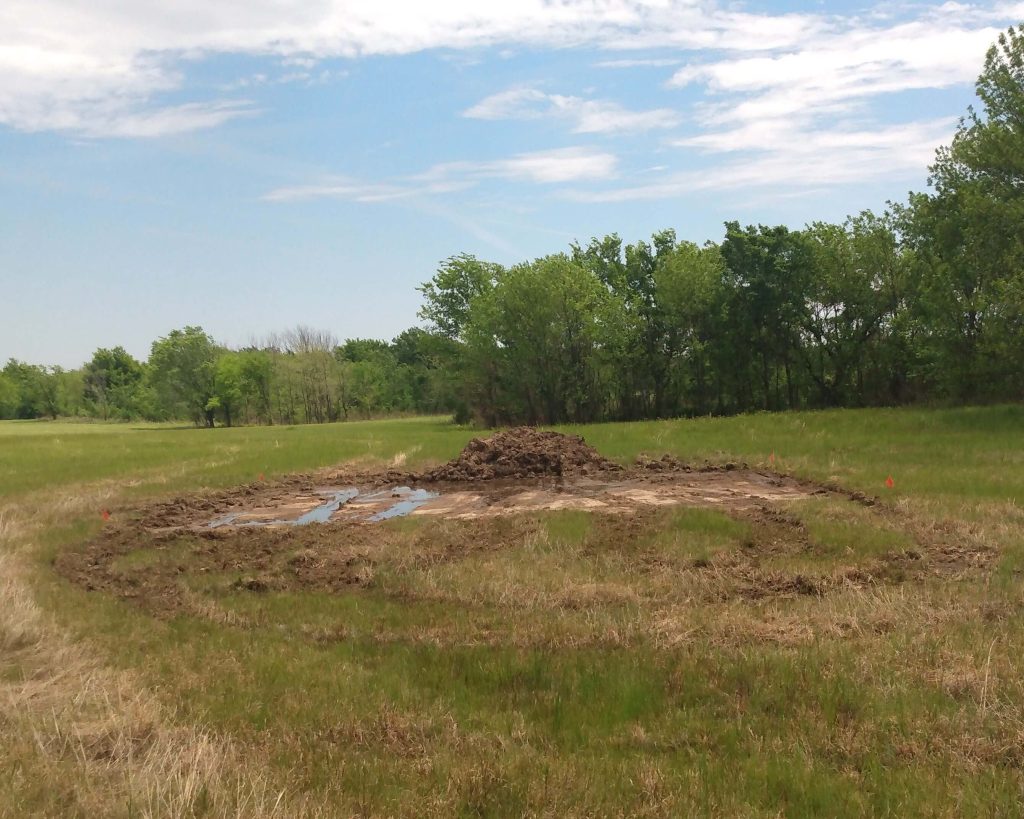A dirt pad marked out on land with water filling the pad. 