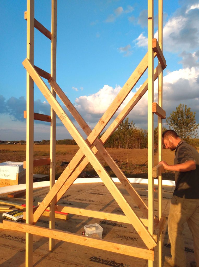 Man situating scaffolding on a round platform with trees and blues skies in the background